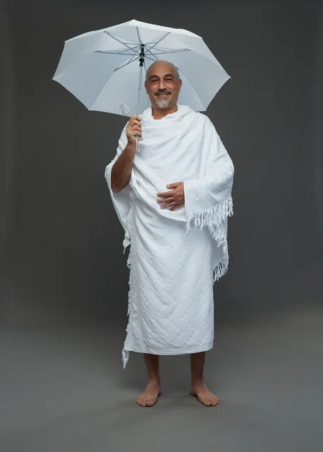 A portrait of a Saudi man in Ihram clothing holding a white umbrella while performing rituals, with various gestures and signals, full body, gray background.