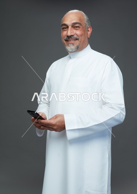 رجل  عربي سعودي خليجي مسن يرتدي الزي الثوب الابيض ويمسك الهاتف المحمول,  ايماءات واشارات مختلفه , كامل الجسم, خلفيه رماديه