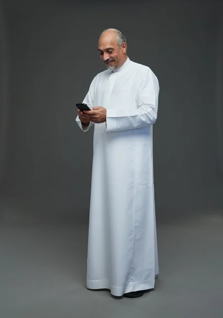 An elderly Arab Saudi Gulf man wearing a white thobe and holding a mobile phone, making various gestures and signals, full body, gray background.