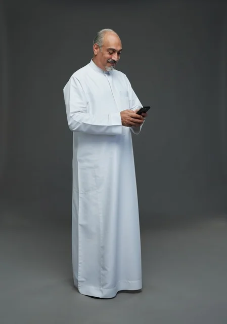 رجل  عربي سعودي خليجي مسن يرتدي الزي الثوب الابيض ويمسك الهاتف المحمول,  ايماءات واشارات مختلفه , كامل الجسم, خلفيه رماديه