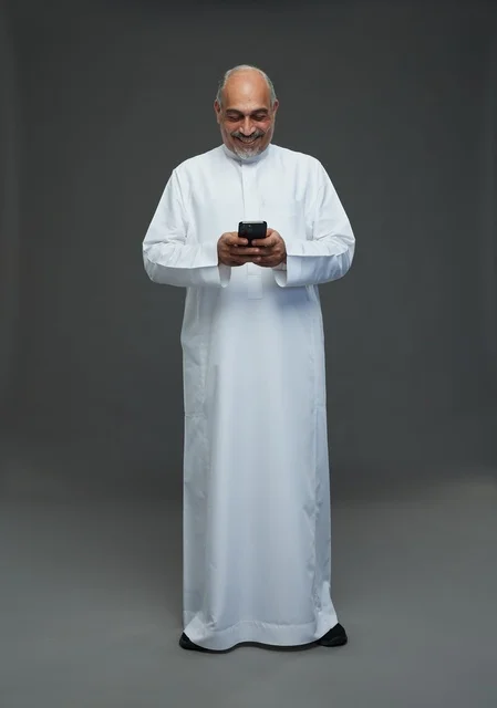 رجل  عربي سعودي خليجي مسن يرتدي الزي الثوب الابيض ويمسك الهاتف المحمول,  ايماءات واشارات مختلفه , كامل الجسم, خلفيه رماديه