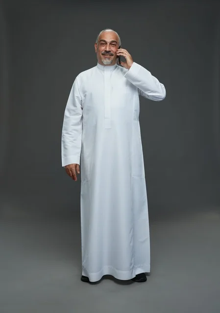 رجل  عربي سعودي خليجي مسن يرتدي الزي الثوب الابيض ويمسك الهاتف المحمول, اجراء مكالمه هاتفيه,  ايماءات واشارات مختلفه , كامل الجسم, خلفيه رماديه