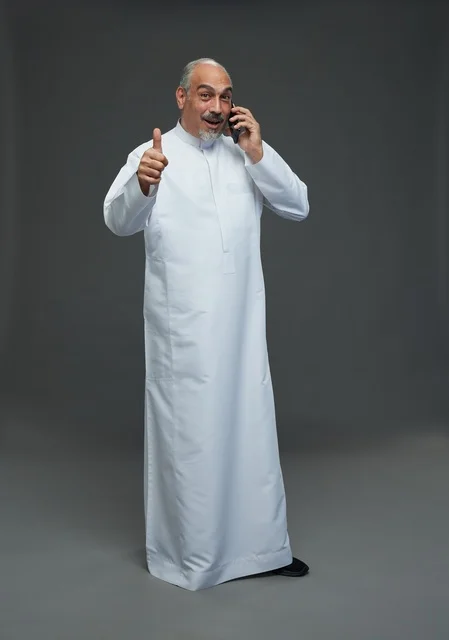 An elderly Arab Saudi Gulf man wearing a white thobe is holding a mobile phone, making a phone call, with various gestures and signals, full body, gray background.