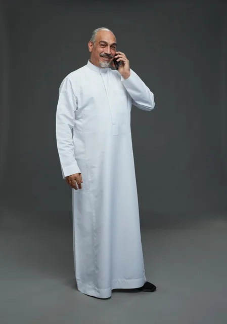 رجل  عربي سعودي خليجي مسن يرتدي الزي الثوب الابيض ويمسك الهاتف المحمول, اجراء مكالمه هاتفيه,  ايماءات واشارات مختلفه , كامل الجسم, خلفيه رماديه