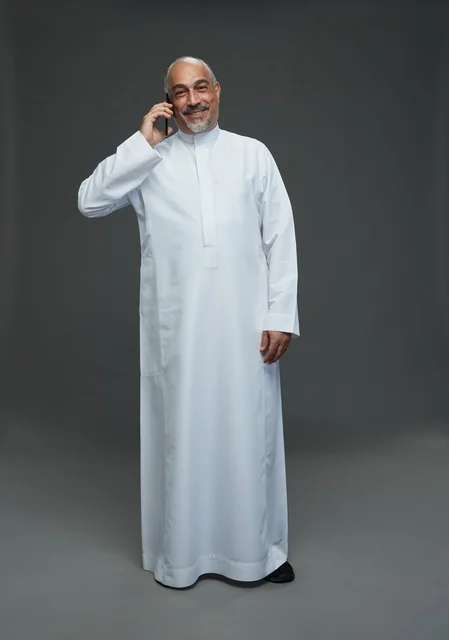 رجل  عربي سعودي خليجي مسن يرتدي الزي الثوب الابيض ويمسك الهاتف المحمول, اجراء مكالمه هاتفيه,  ايماءات واشارات مختلفه , كامل الجسم, خلفيه رماديه