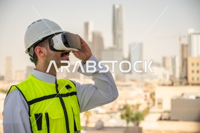  الوظائف الشبابية في المملكة السعودية، نمو وتطور الهندسة المعمارية على ايدي المبدعين أبناء الوطن، صورة جانبية لمهندس عربي خليجي سعودي يرتدي الثوب التقليدي والسترة الخاصة وخوذة الحماية ينظر في نظارة واقع افتراضي ثلاثية الأبعاد، خلفية أبراج وناطحات سحاب 