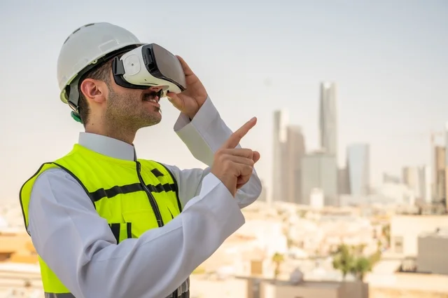  الوظائف الشبابية في المملكة السعودية، نمو وتطور الهندسة المعمارية على ايدي المبدعين أبناء الوطن، صورة جانبية لمهندس عربي خليجي سعودي يرتدي الثوب التقليدي والسترة الخاصة وخوذة الحماية ينظر في نظارة واقع افتراضي ثلاثية الأبعاد، خلفية أبراج وناطحات سحاب 
