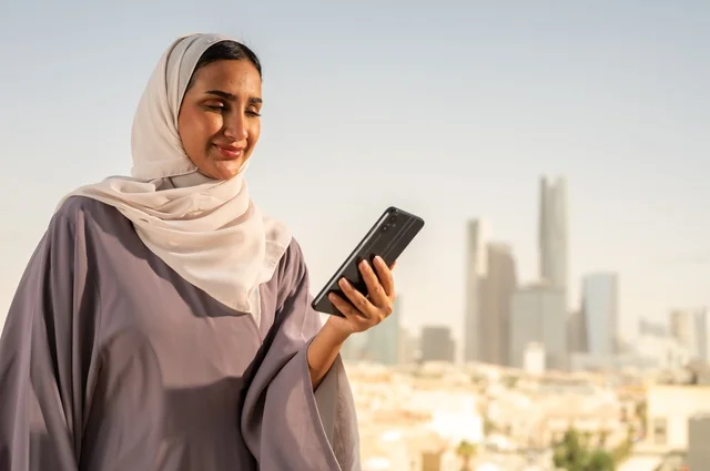 تصفح الانترنت و مواقع التواصل الاجتماعي عبر جهاز الجوال،سيدة عربية خليجية سعودية ترتدي العباءة تقوم باستخدام الهاتف المحمول بايماءات السعادة والسرور،الخروج في الهواء الطلق،التواصل مع الاهل و الاصدقاء