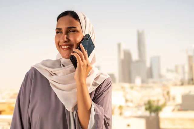 اجراء مكالمة هاتفية عبر جهاز الجوال،صورة مقربة لسيدة عربية خليجية سعودية ترتدي العباءة تقوم باستخدام الهاتف المحمول بايماءات السعادة والسرور،الخروج في الهواء الطلق،التواصل مع الاهل و الاصدقاء