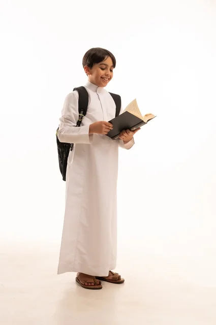 أهمية القراءة في توسيع آفاق المعرفة وزيادة المعلومات، الاجتهاد للوصول إلى النجاح، المناهج العلمية التعليمية، مفهوم العودة إلى المدارس، بورتريه لطالب عربي خليجي سعودي يرتدي الثوب التقليدي يحمل حقيبة الظهر المدرسية ويحمل بيده كتاب، صورة لكامل الجسم، خلفية بيضاء
