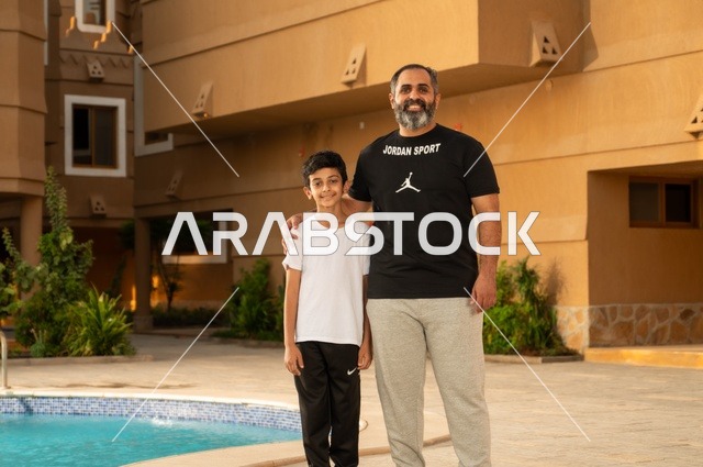 قضاء العطلة الصيفية في المنتجعات السياحية, مشاركة العائلة اللحظات الممتعة, القيام بالأنشطة الترفيهية المسلية, اب عربي خليجي سعودي يقف بجانب حوض السباحة مع ولده في إحدى الفنادق بالسعودي، ممارسة رياضة السباحة الممتعة