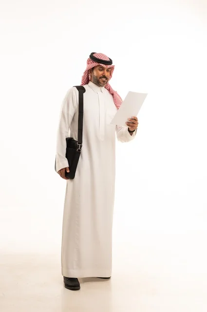 قراءة وتدقيق الملاحظات، مفهوم إداة الأعمال والمشاريع، الاستعداد للذهاب إلى العمل، بورتريه لرجل عربي خليجي سعودي يرتدي الثوب التقليدي والشماغ يحمل بيده حقيبة يد وورقة بيضاء، الأناقة والاهتمام بالمظهر الخارجي، الجسم بالطول الكامل، خلفيه بيضاء