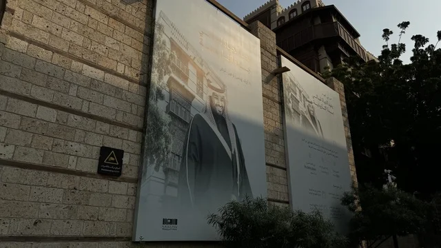 لافتة باللون الأبيض والأسود معلقة على جدار حجري، الفنون المعمارية في المدينة التاريخية في جدة، تصوير درون للحارات والتصاميم الشعبية، الأماكن السياحية في المملكة العربية السعودية، المباني الأثرية القديمة، مشاريع إعادة إحياء المنطقة