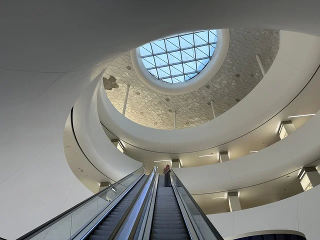 صورة من الداخل لسيدة تصعد على درج مركز اثراء، 5 أكتوبر 2025، مكان للقراء ومحبي العلم والكتب والمعرفة، أكبر المكتبات العامة في السعوديه، مركز الملك عبد العزيز الثقافي العالمي (إثراء) في مدينة الظهران في المملكة العربية السعودية, كتب و روايات وقصص مرتبة في الرفوف.