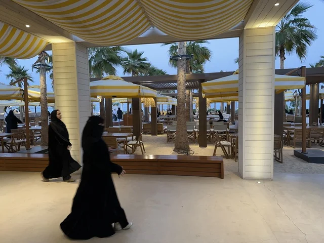 An exterior design with striped fabric canopies in yellow and white, Solt Al-Bahr is a family-friendly recreational and beach destination located on the Corniche Road in Khobar, Saudi Arabia. Additional renovations and developments are set for January 3, 2026, featuring a sandy beach with umbrellas and palm trees.