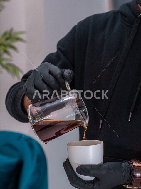 A waiter wearing black gloves pours coffee into a cup, prepares and serves hot drinks, espresso coffee
