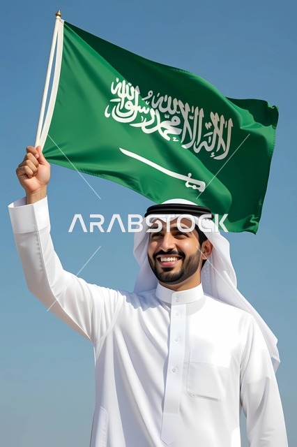 رفع علم المملكة للأعلى ، النظر إلى شيئ ما بإيماءات السرور والفرح ،بورتريه مقرب لرجل عربي خليجي سعودي يرتدي الزي التقليدي السعودي، مفهوم الاهتمام في المظهر الخارجي
