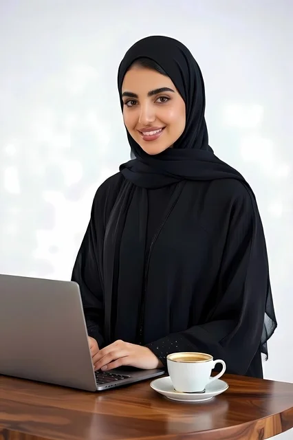 The concept of remote work, using a modern and advanced technical device, a portrait of a Saudi Arabian Gulf woman wearing a black abaya and a hijab working on a laptop with a cup of coffee beside her, accomplishing tasks and work, white background.