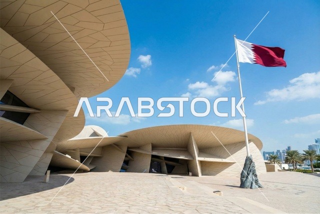 علم دولة قطر يرفرف في السماء الزرقاء, الاحتفال باليوم الوطني القطري, المتحف الوطني الإسلامي للفنون في العاصمة القطرية الدوحة, معالم سياحية مشهورة في وقت النهار، المباني الطينية على الطراز القديم