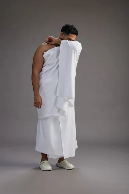 A portrait of a Saudi man in Ihram clothing sneezing and respectfully covering his mouth, the concept of Hajj and Umrah, full-body, gray background. A portrait of a Saudi man in Ihram clothing sneezing and respectfully covering his mouth, the concept of Hajj and Umrah, full-body, gray background.