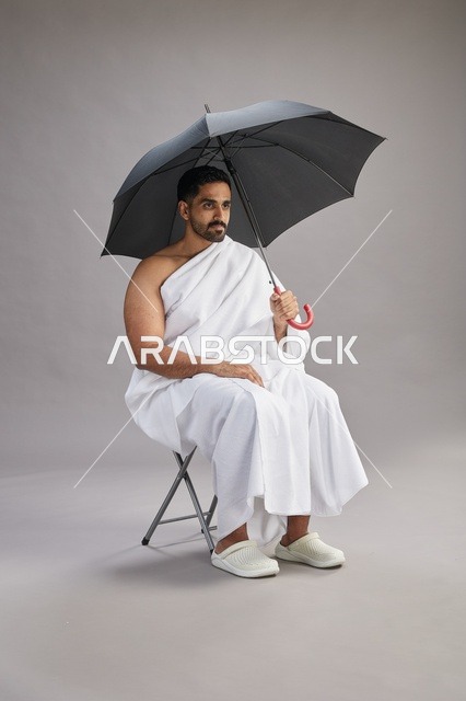 رجل سعودي بملابس الإحرام يمسك مظلة في الاستوديو