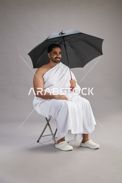 رجل سعودي بملابس الإحرام يحمل مظلة في الاستوديو