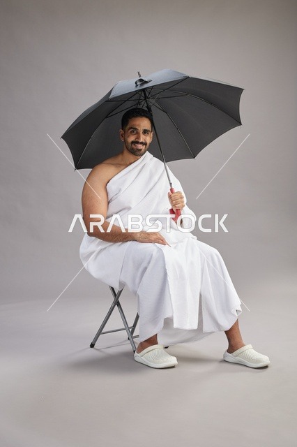 رجل سعودي بملابس الإحرام يحمل مظلة في الاستوديو