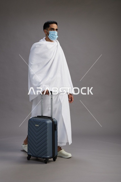 حاج عربي بملابس الإحرام مع حقيبة سفر وكمامة
