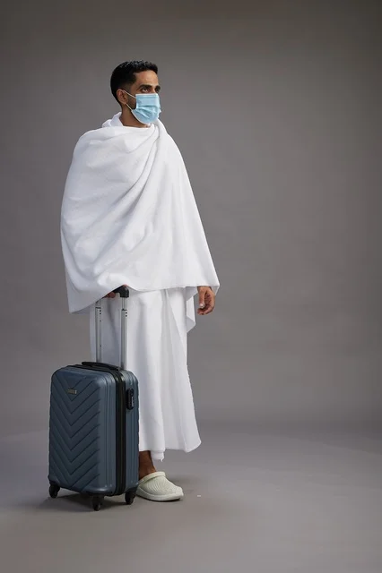 رجل سعودي بملابس الإحرام مع حقيبة سفر وكمامة طبية