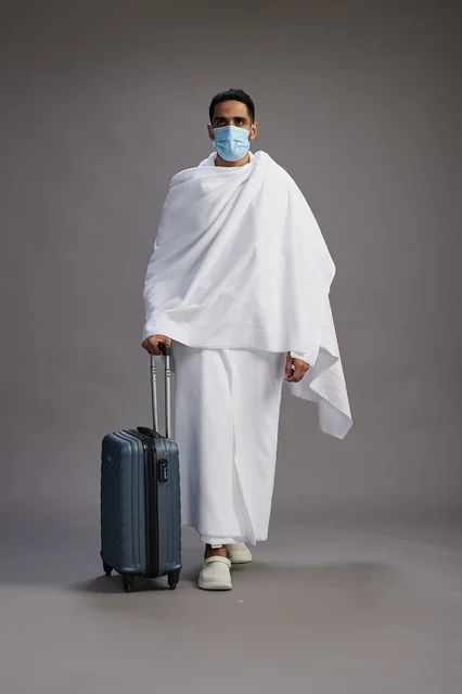 حاج سعودي بملابس الإحرام مع حقيبة سفر وكمامة
