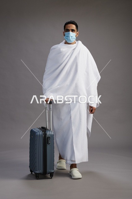رجل سعودي بملابس الإحرام مع حقيبة سفر وكمامة طبية