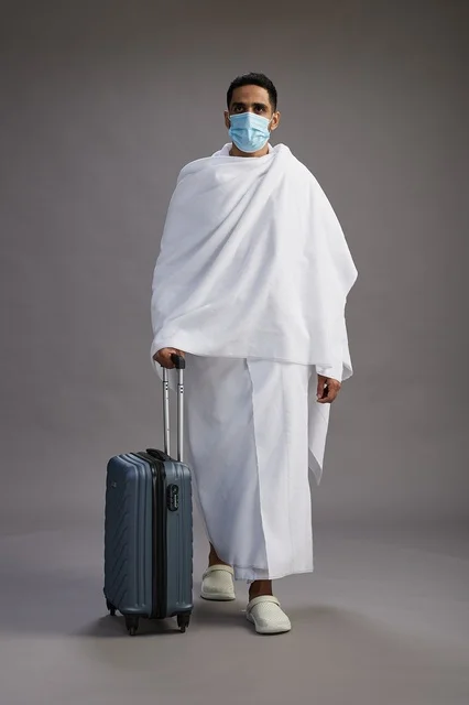 رجل سعودي بملابس الإحرام مع حقيبة سفر وكمامة طبية