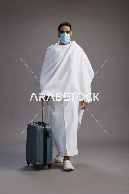 رجل سعودي بملابس الإحرام والكمامة مع حقيبة سفر
