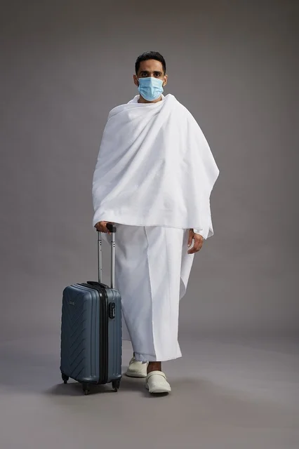 رجل سعودي بملابس الإحرام والكمامة مع حقيبة سفر