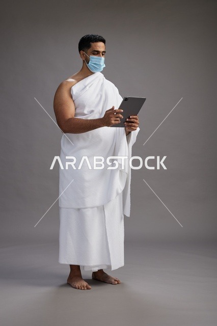 حاج بملابس الإحرام يحمل تابلت ويرتدي كمامة