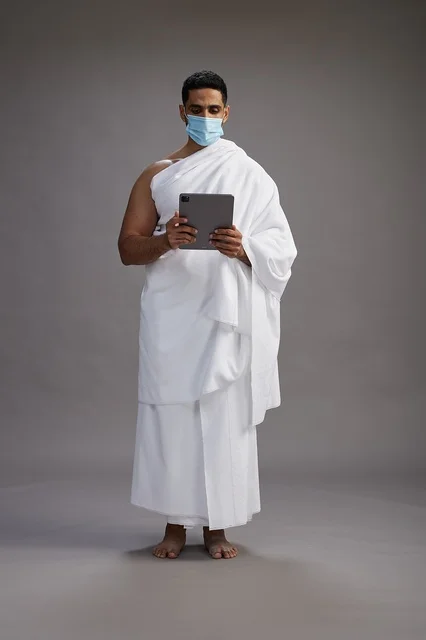 رجل عربي بملابس الإحرام مع كمامة وجهاز لوحي