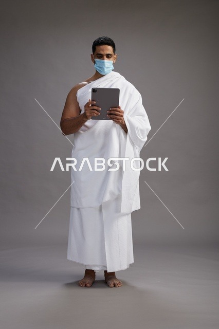Pilgrim in ihram holding tablet and wearing face mask