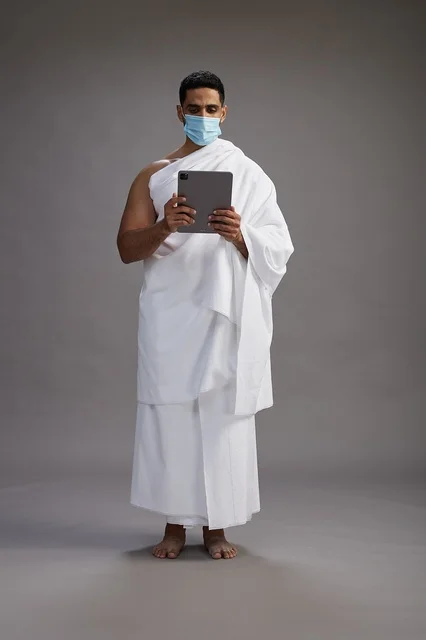 حاج بملابس الإحرام يحمل تابلت ويرتدي كمامة