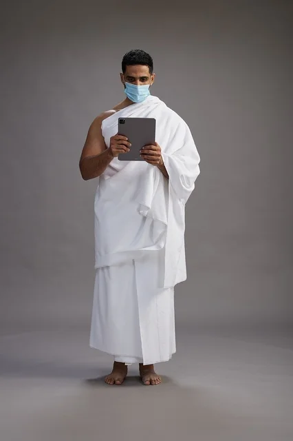 رجل سعودي بملابس الإحرام يستخدم تابلت مع كمامة