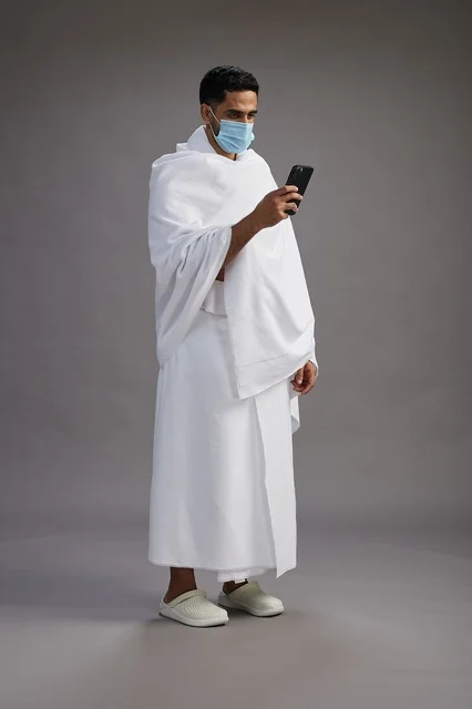 رجل سعودي بملابس الإحرام والكمامة يستخدم الجوال