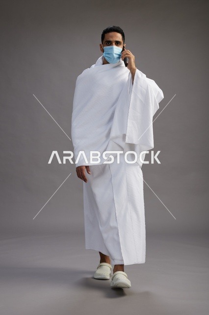رجل سعودي بملابس الإحرام يستخدم الجوال مع كمامة