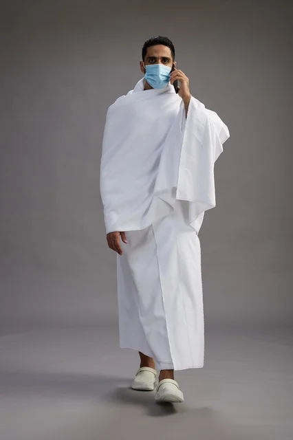 رجل سعودي بملابس الإحرام يستخدم الجوال مع كمامة