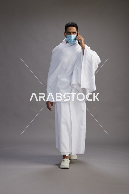 Arab Pilgrim in Ihram Wearing Face Mask Using Mobile Phone