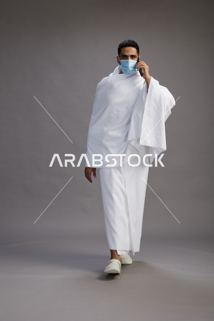 رجل سعودي بملابس الإحرام يتحدث بالهاتف مع كمامة