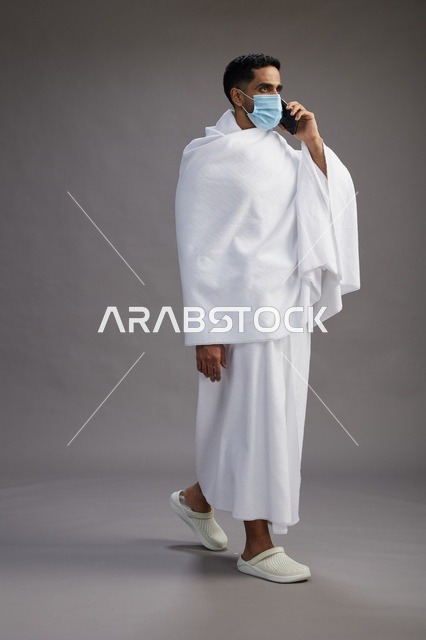 رجل سعودي بملابس الإحرام يستخدم الجوال مع كمامة