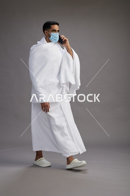 حاج سعودي بملابس الإحرام يستخدم الجوال بالكمامة