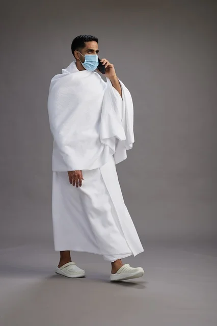 حاج سعودي بملابس الإحرام يستخدم الجوال بالكمامة