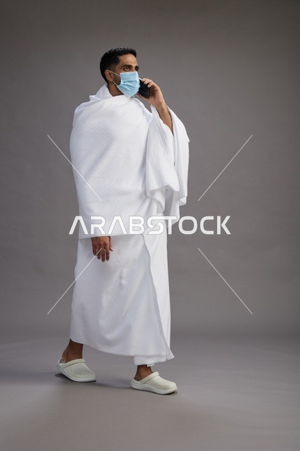 معتمر سعودي بملابس الإحرام يتحدث بالجوال مع كمامة