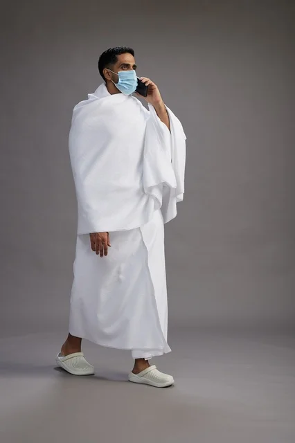 معتمر سعودي بملابس الإحرام يتحدث بالجوال مع كمامة