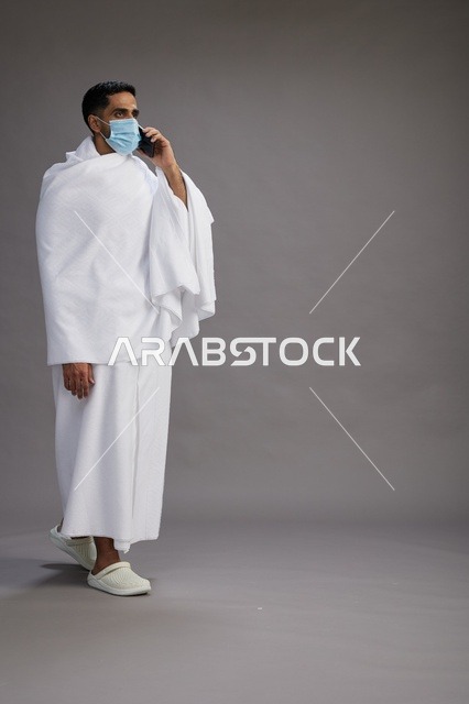 رجل سعودي بملابس الإحرام والكمامة يتحدث بالهاتف